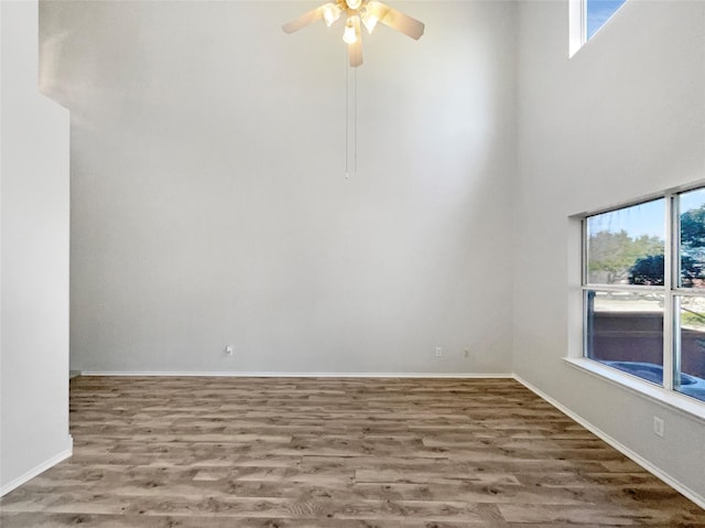 spare room with hardwood / wood-style flooring, a towering ceiling, a wealth of natural light, and ceiling fan