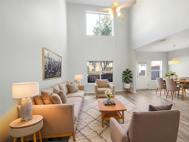 living room with ceiling fan, light hardwood / wood-style floors, a healthy amount of sunlight, and a high ceiling