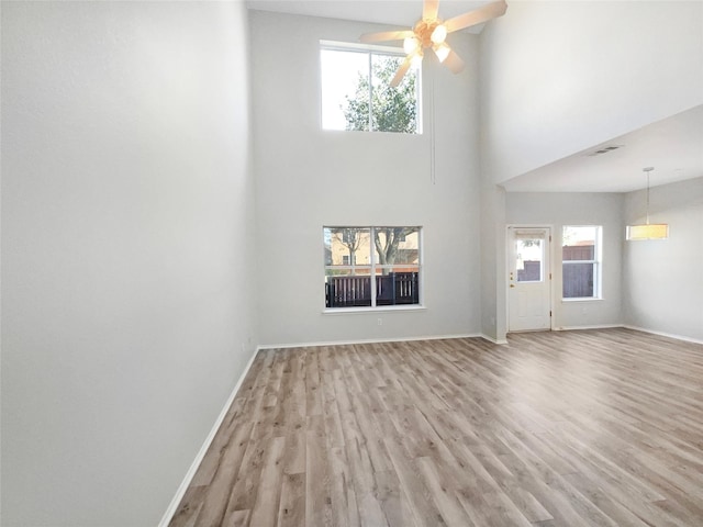 unfurnished living room with a towering ceiling, a healthy amount of sunlight, ceiling fan, and light hardwood / wood-style flooring