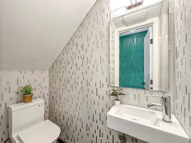 bathroom with vaulted ceiling, tasteful backsplash, sink, tile walls, and toilet