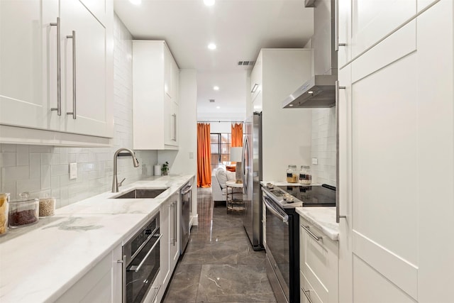 kitchen with white cabinetry, sink, light stone counters, stainless steel appliances, and wall chimney range hood