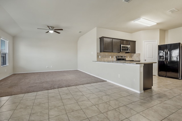 kitchen with appliances with stainless steel finishes, backsplash, kitchen peninsula, light stone countertops, and dark brown cabinets