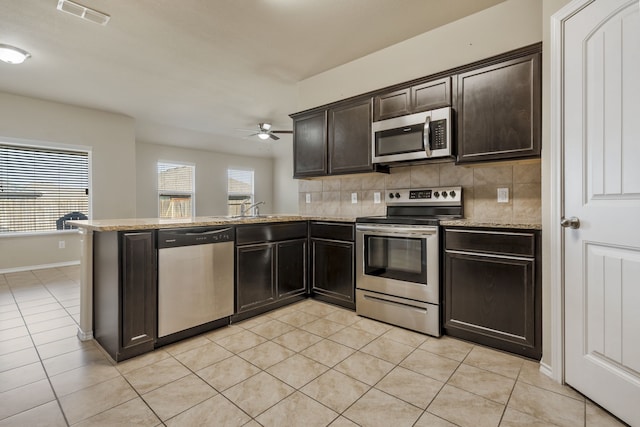 kitchen with light stone counters, backsplash, stainless steel appliances, and kitchen peninsula