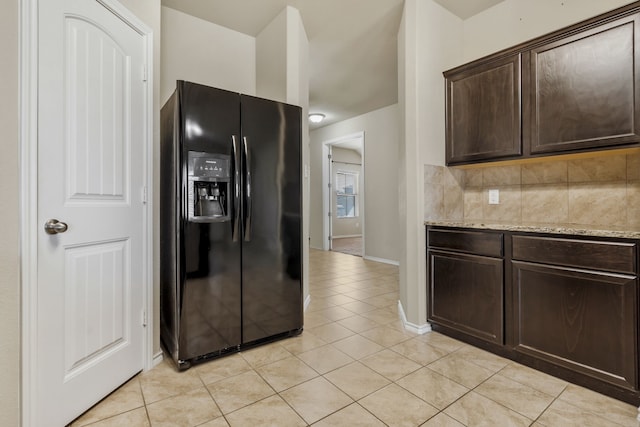 kitchen featuring backsplash, dark brown cabinets, light stone counters, light tile patterned flooring, and black fridge with ice dispenser