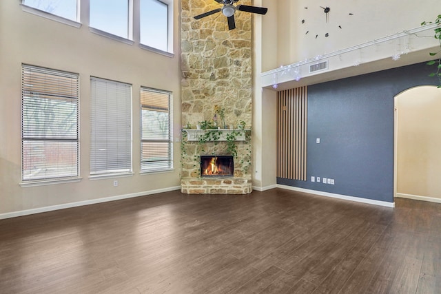 unfurnished living room featuring dark hardwood / wood-style floors, ceiling fan, a stone fireplace, and a towering ceiling