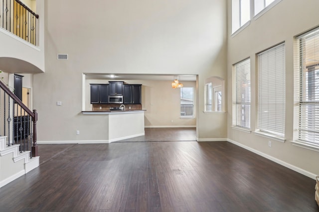 unfurnished living room featuring dark wood-type flooring, a notable chandelier, and a towering ceiling