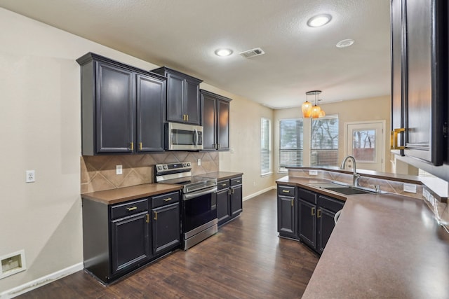 kitchen with sink, appliances with stainless steel finishes, hanging light fixtures, dark hardwood / wood-style floors, and tasteful backsplash