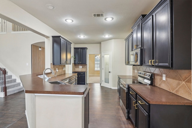 kitchen with sink, dark hardwood / wood-style floors, kitchen peninsula, stainless steel appliances, and backsplash