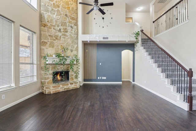 unfurnished living room featuring ceiling fan, a towering ceiling, a fireplace, and dark hardwood / wood-style flooring