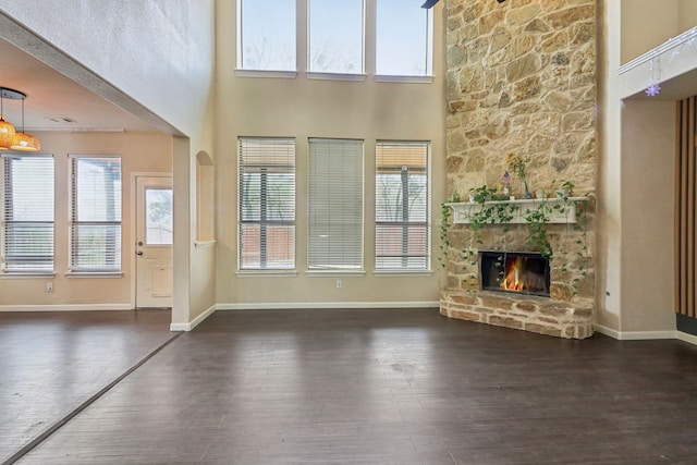 unfurnished living room featuring dark wood-type flooring, a fireplace, a towering ceiling, and plenty of natural light