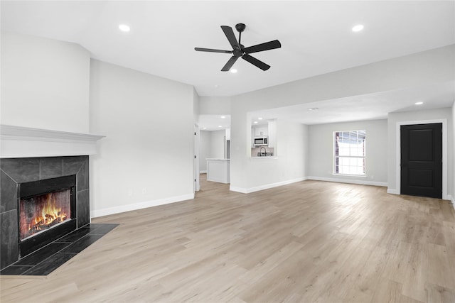 unfurnished living room with a tile fireplace, ceiling fan, and light hardwood / wood-style floors