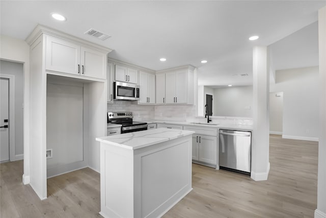 kitchen featuring appliances with stainless steel finishes, white cabinets, light stone counters, and decorative backsplash