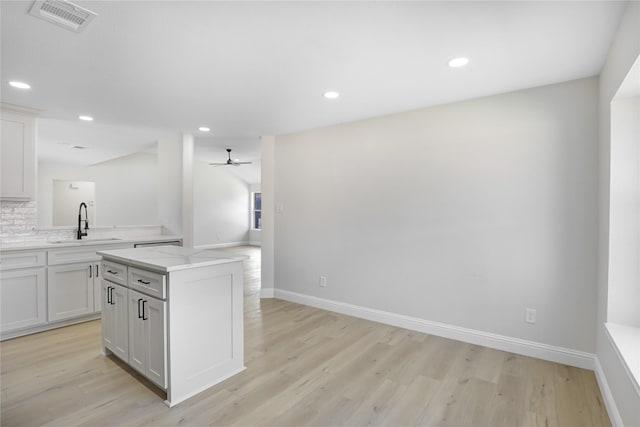 kitchen featuring sink, white cabinets, a center island, light stone counters, and light wood-type flooring