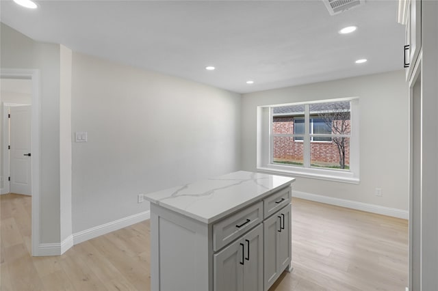 kitchen with gray cabinetry, light wood-type flooring, light stone countertops, and a kitchen island