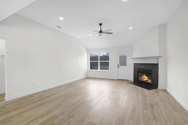 unfurnished living room with a tiled fireplace, vaulted ceiling, ceiling fan, and light hardwood / wood-style flooring