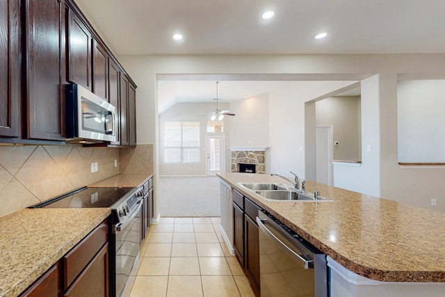 kitchen with sink, stainless steel appliances, decorative backsplash, a center island with sink, and a stone fireplace