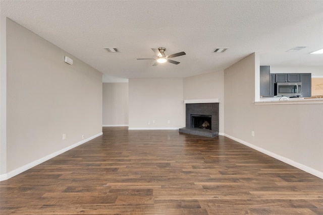 unfurnished living room with ceiling fan, a brick fireplace, a textured ceiling, and dark hardwood / wood-style flooring