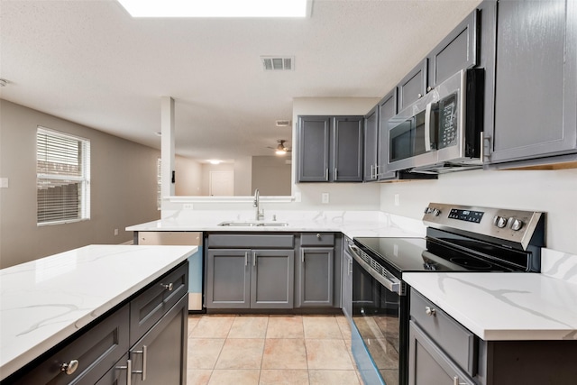 kitchen with appliances with stainless steel finishes, gray cabinets, light stone countertops, and sink