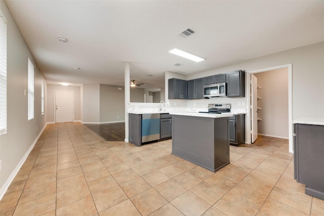 kitchen with light tile patterned floors, gray cabinets, ceiling fan, appliances with stainless steel finishes, and a center island