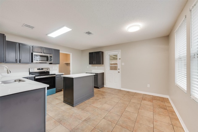 kitchen featuring sink, a textured ceiling, light tile patterned floors, appliances with stainless steel finishes, and a kitchen island