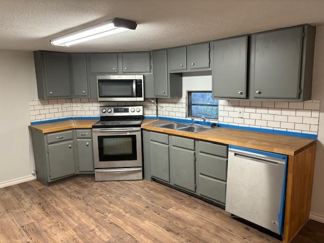 kitchen with butcher block counters, sink, appliances with stainless steel finishes, hardwood / wood-style flooring, and backsplash