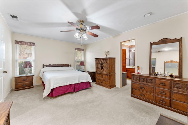 bedroom with ensuite bathroom, light colored carpet, and ceiling fan