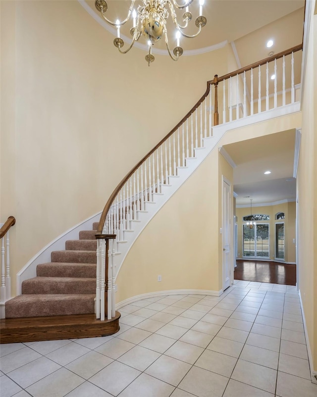 staircase with ornamental molding, a towering ceiling, a notable chandelier, and tile patterned floors