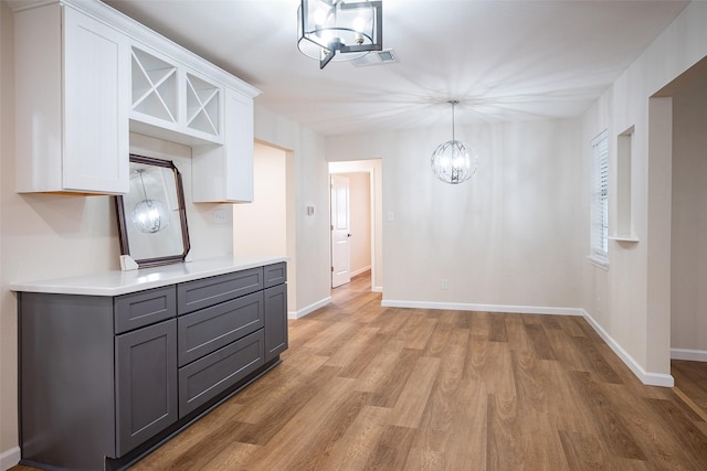 kitchen with light wood-type flooring, gray cabinets, a notable chandelier, pendant lighting, and white cabinets