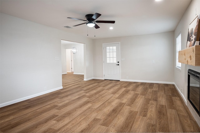 unfurnished living room featuring ceiling fan with notable chandelier and light hardwood / wood-style flooring