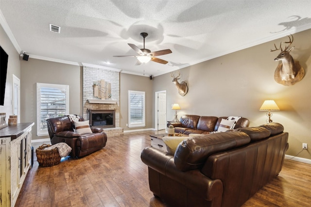 living room with crown molding, a textured ceiling, dark hardwood / wood-style flooring, ceiling fan, and a fireplace