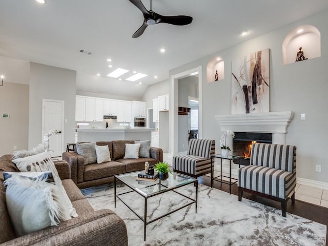 living room featuring lofted ceiling with skylight, ceiling fan, and light wood-type flooring