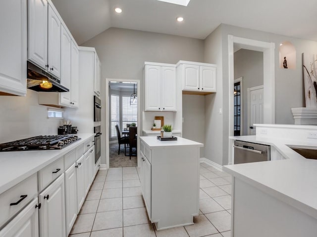 kitchen with light tile patterned flooring, under cabinet range hood, stainless steel appliances, a kitchen island, and vaulted ceiling