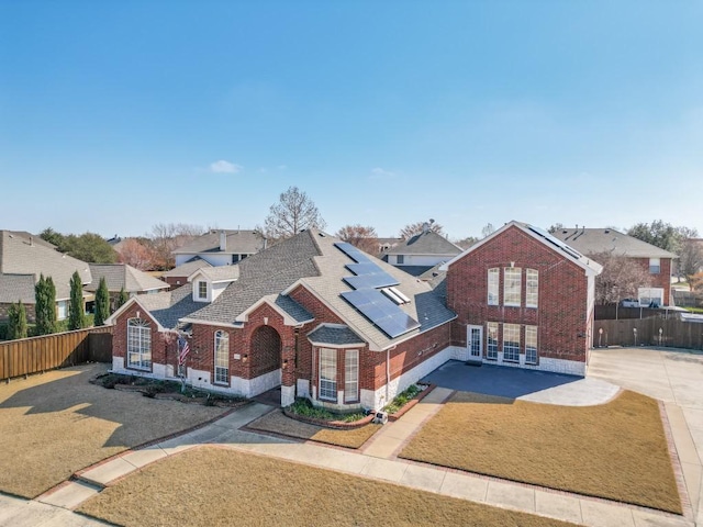 view of front of home with a shingled roof, brick siding, fence, and solar panels