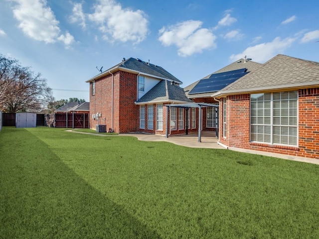 rear view of property with a patio, a yard, a shed, and solar panels