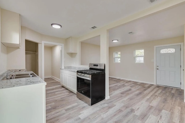 kitchen featuring sink, light hardwood / wood-style flooring, white cabinetry, light stone counters, and gas range