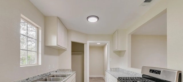 kitchen featuring white cabinetry, sink, stainless steel range, light stone counters, and light wood-type flooring