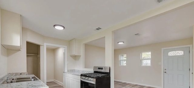 kitchen with light stone counters, stainless steel gas range, sink, and white cabinets