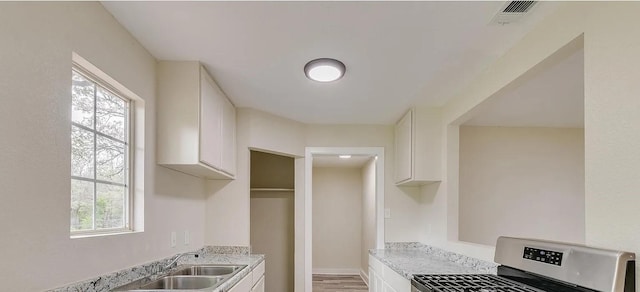 kitchen with white cabinetry, sink, light stone countertops, and stainless steel range oven