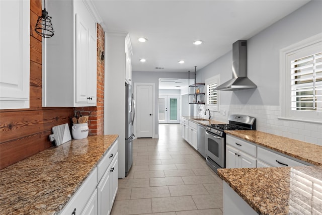 kitchen featuring pendant lighting, wall chimney range hood, appliances with stainless steel finishes, dark stone countertops, and white cabinets