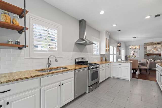 kitchen featuring sink, white cabinetry, hanging light fixtures, stainless steel appliances, and wall chimney range hood