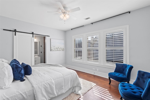 bedroom featuring ensuite bath, wood-type flooring, a barn door, and ceiling fan