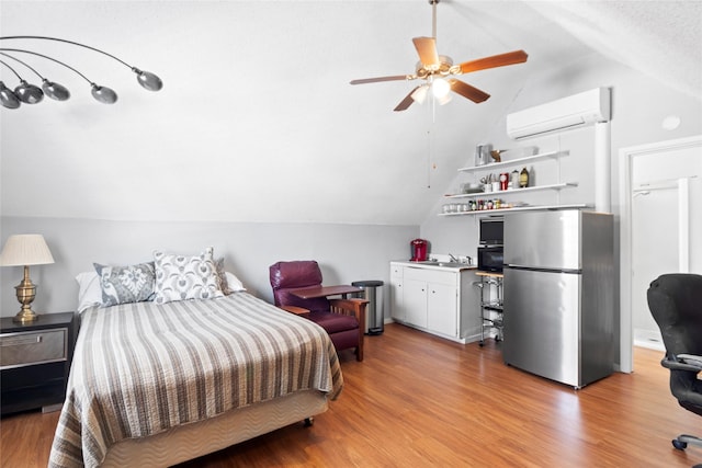 bedroom featuring vaulted ceiling, a wall mounted AC, stainless steel refrigerator, and light hardwood / wood-style flooring