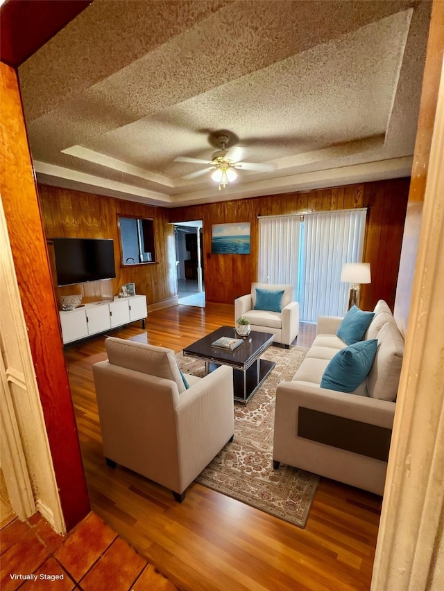 living room featuring a textured ceiling, wood-type flooring, a raised ceiling, and wooden walls