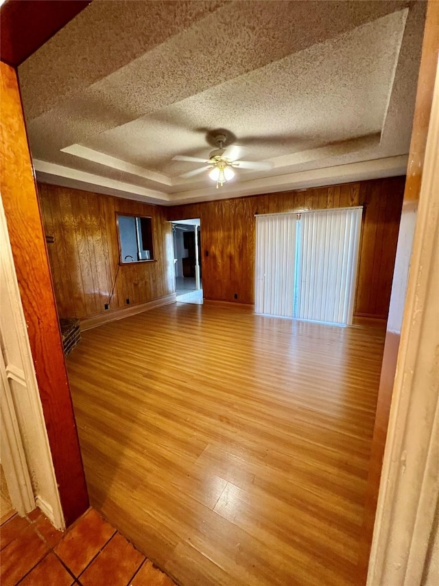 empty room with hardwood / wood-style floors, wood walls, ceiling fan, a tray ceiling, and a textured ceiling