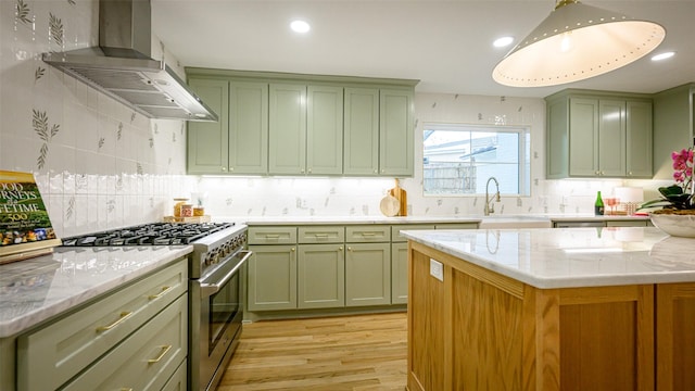 kitchen featuring wall chimney range hood, sink, light stone counters, high end stainless steel range, and green cabinetry