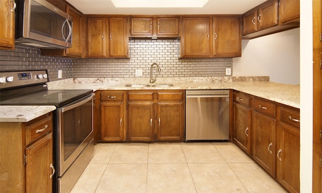 kitchen with appliances with stainless steel finishes, sink, decorative backsplash, light tile patterned floors, and light stone countertops