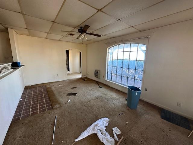 unfurnished living room featuring heating unit, a drop ceiling, and ceiling fan