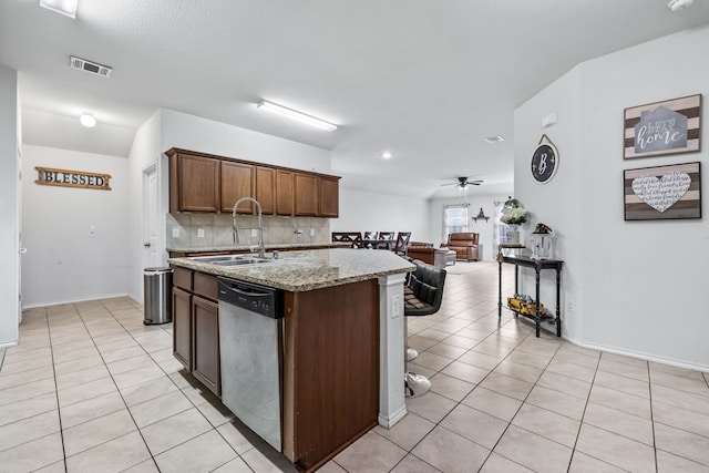 kitchen featuring sink, light stone countertops, an island with sink, light tile patterned flooring, and stainless steel dishwasher