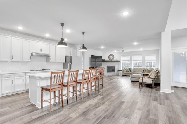 kitchen featuring white cabinetry, decorative backsplash, hanging light fixtures, white fridge, and a center island with sink