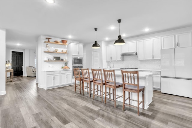 kitchen with stainless steel appliances, light hardwood / wood-style floors, white cabinets, a center island with sink, and decorative light fixtures